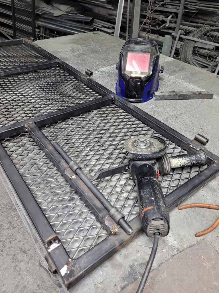 Picture of a table in a workshop. There's a metal door frame, a grinder and a welder's mask on the table.