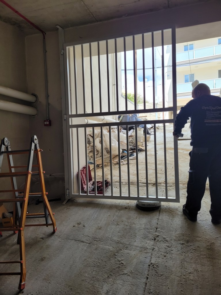 Picture taken from inside the garage facing outside. You can see a ladder on the left, and a man working on a metal door on the right.