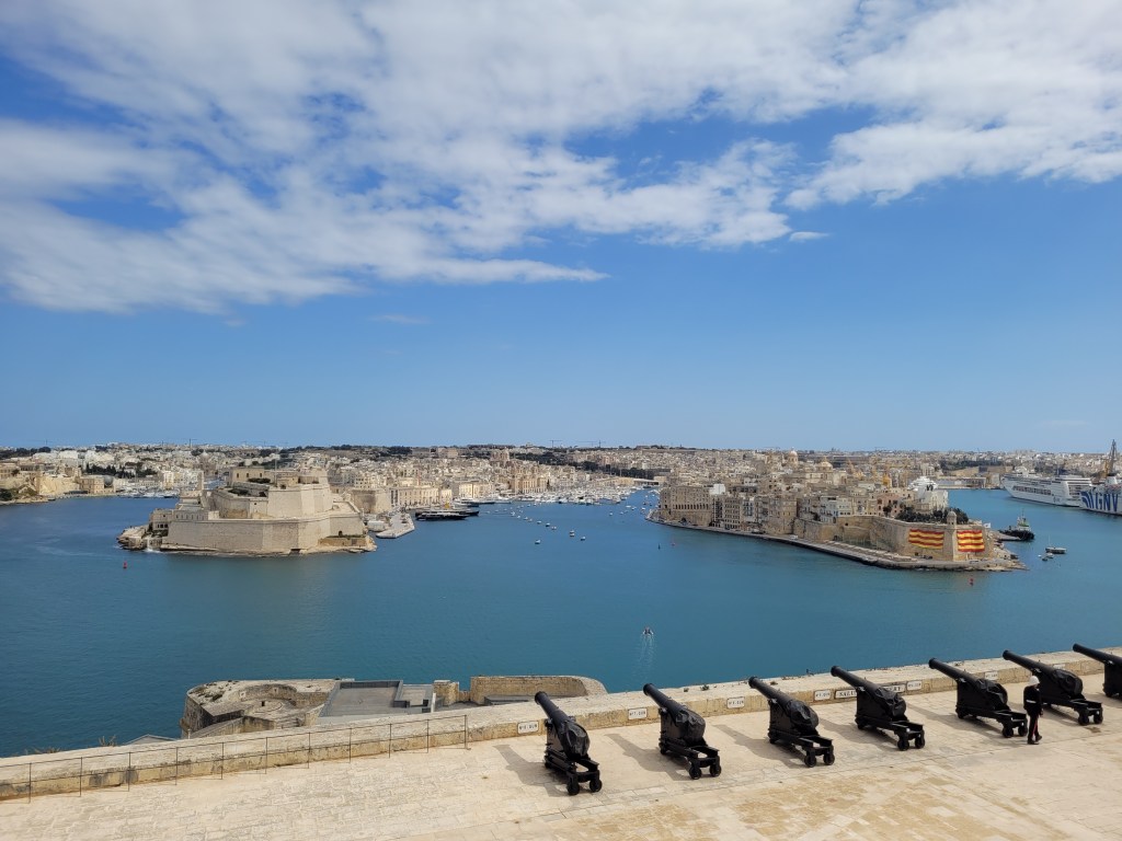 Landscape picture from Valletta showing cannons facing the ocean and another part of the city in the background across the bay.