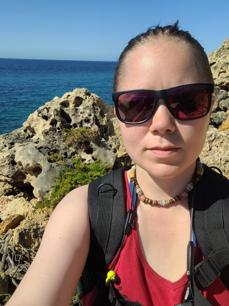 Selfie of a woman with a backpack on a rocky coast of Gozo island