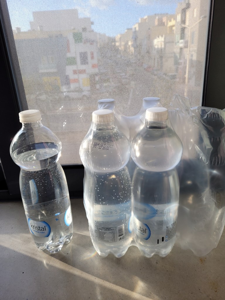 Picture of a plastic-wrapped pack of bottled water with one bottle out of the back.   