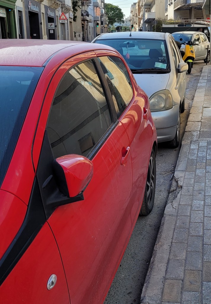 Picture with a street of parked cars. The first car has its side view mirror pulled in so as to not stick out of the car.