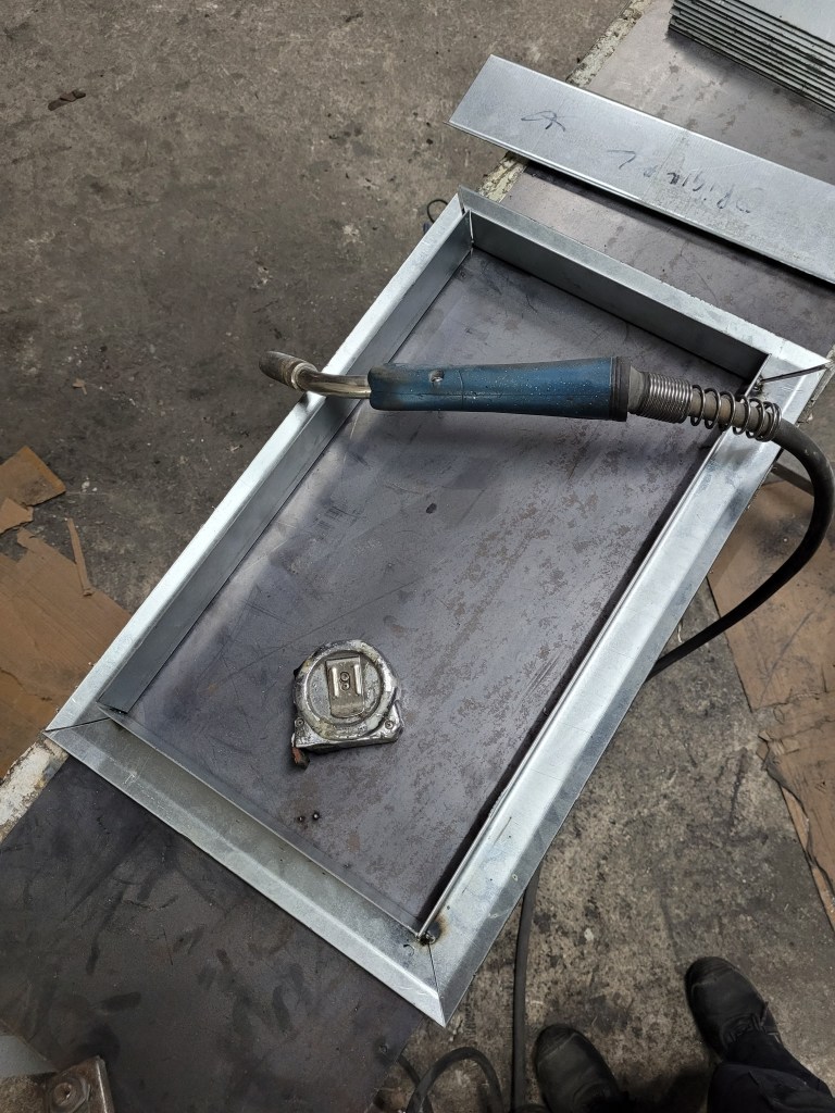 Picture of a welded rectangular metal frame with a welding machine and a measuring tape