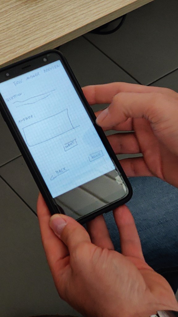 käsi ja kännykkä, jossa näkyy mobiilisovelluksen prototyyppi