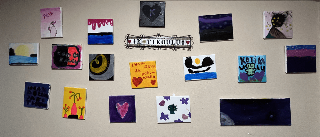 Kuva taideseinästä missä näkyy värikkäitä käsintehtyjä piirustuksia ja kotikoulu merkki niitten keskellä.
