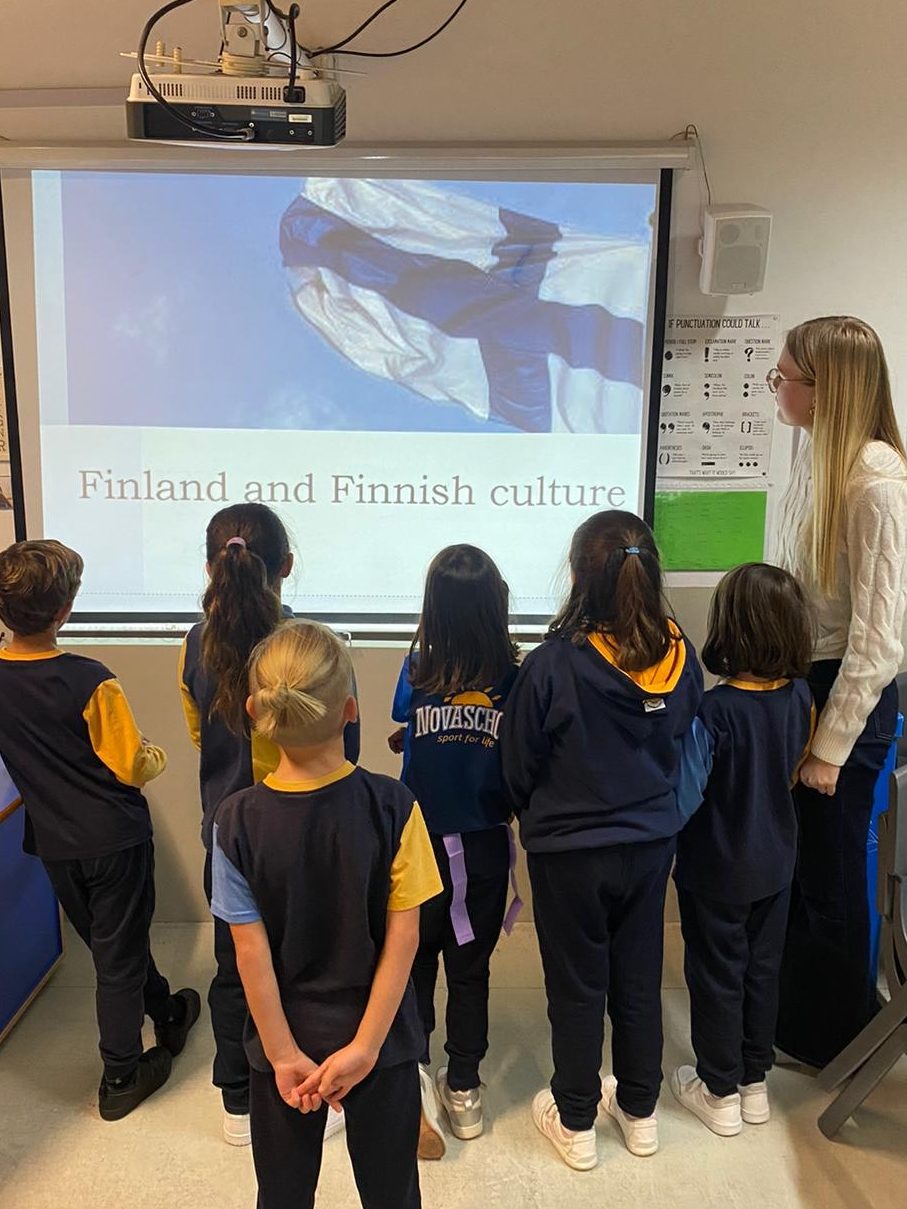 A young woman and students looking at a screen that is showing a presentation about Finland.