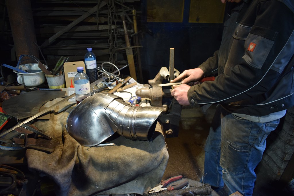 Kuvassa viilataan miekan kahvan osaa. Pöydällä on myös miekka ja osa haarinskaa.