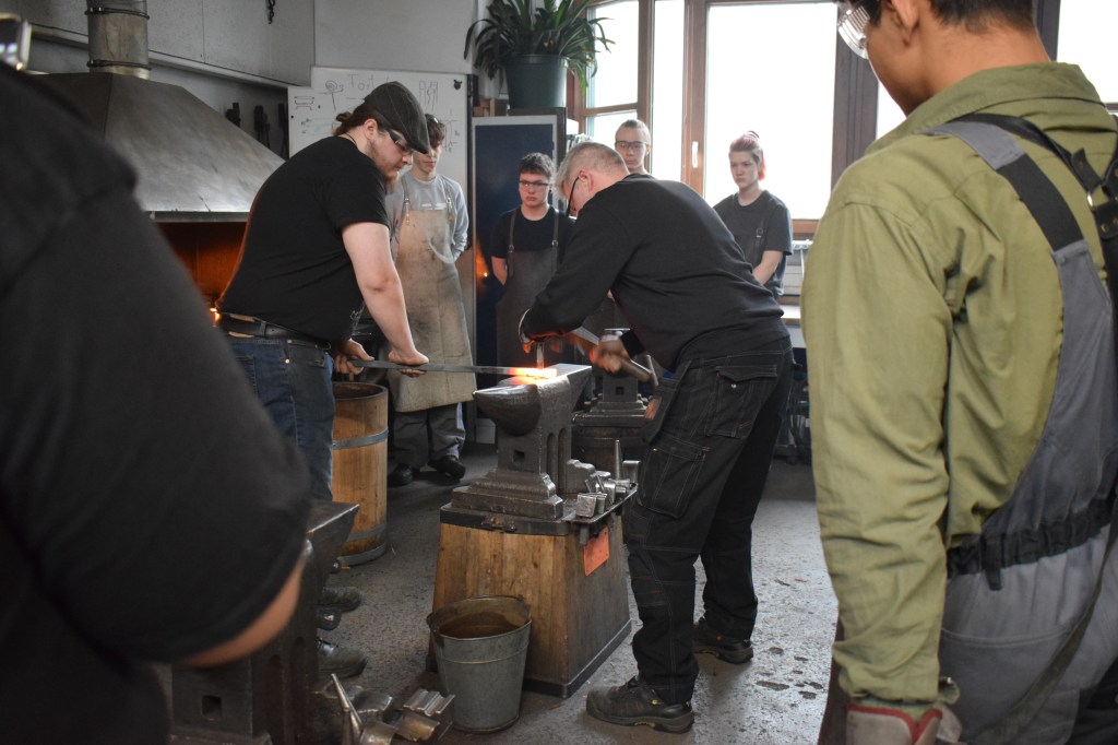 Kuvassa seppämestari Mikko Flemming näyttää kirveen silmäreiän puhkaisua taltalla.