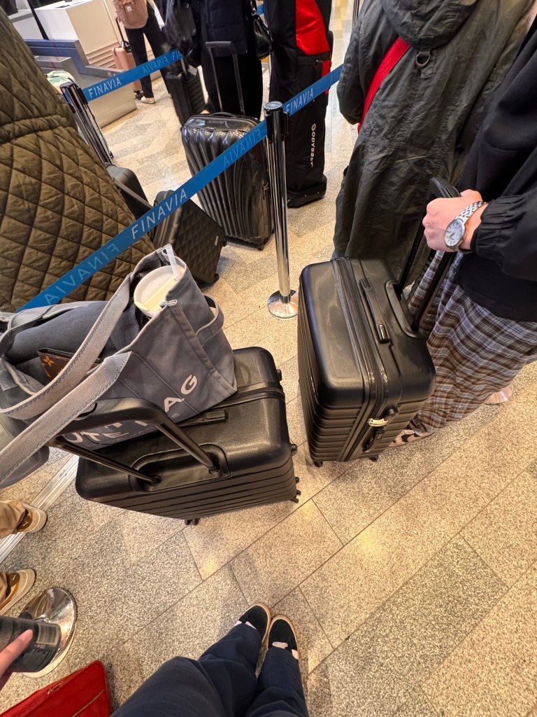 Kuvassa seisomme jonottamassa laukkujen luovutusta. Kuvassa näkyy 2 matkalaukkua. 