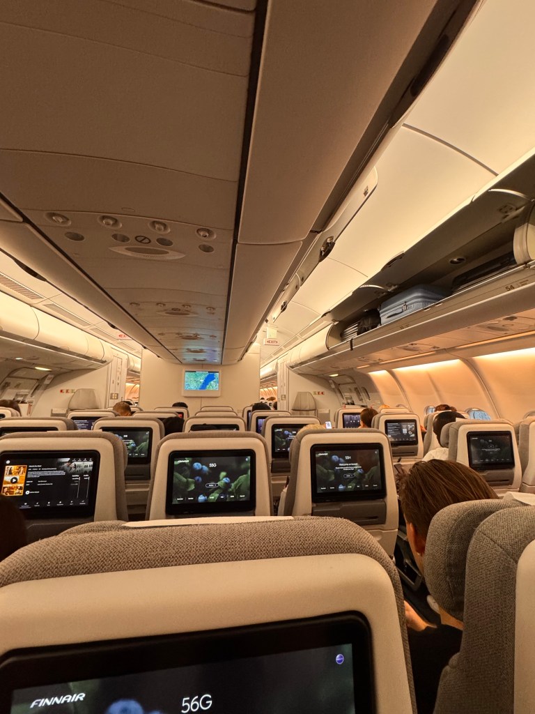 Kuva on lentokoneesta. Kuvassa näkyy penkkejä joissa on näyttö. 