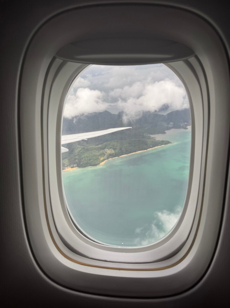 Kuva lentokoneen ikkunasta. Kuvassa näkyy ranta ja turkoosia vettä. 