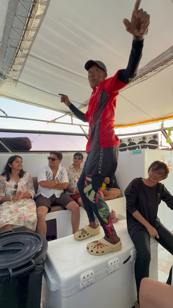 Kuvassa on paljon ihmisiä veneessä ja yksi tanssii tason päällä. 