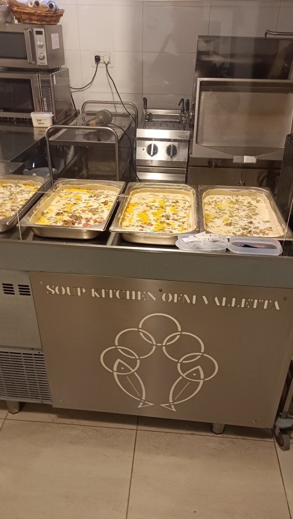 Teräspintaisen suurtalouskeittiön teräsvuokia rivissä pöydällä, joissa paistamista vailla olevat piirakkat odottaa uunia.